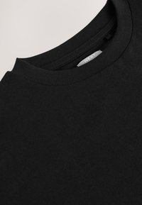 Schwarzes Baumwoll-T-Shirt mit Rundhalsausschnitt, mit glatter Textur und minimalem Branding auf dem Etikett im Nackeninneren.