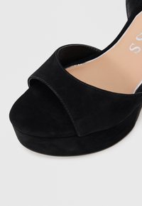 Zwarte suède platform sandaal met open teen, brede voorband en beige binnenzool.