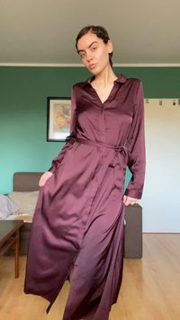 Burgundijska satenasta obleka z dolgimi rokavi, spredaj na gumbe in z pasom v pasu. Ponaša se z lahkotno silhueto in stranskimi žepi. Gladek tekstura.