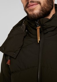 Sort dunjakke med høj krave og en aftagelig hætte. Har en for-lynlås og brune snore detaljer, med blankt foret.