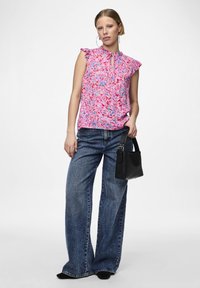 Top senza maniche floreale in rosa con motivi blu e rossi, abbinato a jeans a gamba larga blu e una piccola borsa nera.