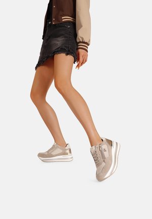 Sneakers in tessuto beige con accenti metallici, design con lacci, suola a strati e dettagli di luccichio sottili, abbinati a una gonna di jeans nera.