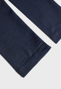 Marineblå bomullleggings med en jevn tekstur, med en tettsittende design og oppbrettede ermer. Nærbilde av benåpningene.