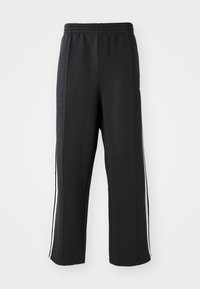 Black sweatpants with an elastic waistband, featuring white side stripes and a relaxed fit. Made from soft, stretchy fabric.