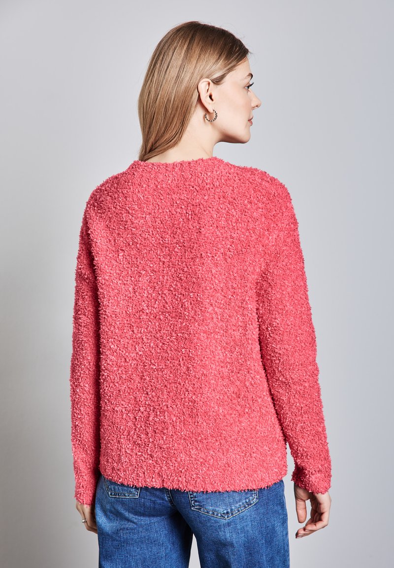 Kanciasty różowy sweter z puszystej, teksturowanej tkaniny, z długimi rękawami i okrągłym dekoltem. Widok z tyłu ukazuje luźny krój.
