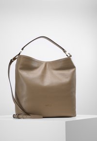 Bolso tote de cuero color marrón claro con una superficie suave y texturizada. Presenta un solo asa superior y una correa de hombro ajustable y desmontable. Acento del logo en dorado.