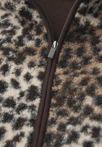 Fleecejacka med leopardmönster som har en brun dragkedja och detaljer, med en mjuk textur i nyanser av brunt, kräm och svart.