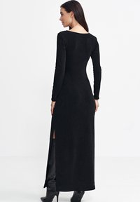 Czarna, prążkowana sukienka maxi z długimi rękawami, z wysokimi bocznymi rozcięciami i zaokrąglonym dekoldem, wykonana z miękkiego, elastycznego materiału.