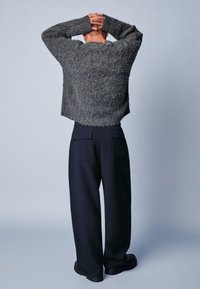 Szary sweter o fakturowanej powierzchni z krótkim, skróconym fasonem, zestawiony z luźnymi czarnymi spodniami z tylnymi kieszeniami oraz solidnymi czarnymi butami.