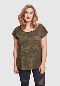 Kamuflasje trykk t-skjorte i olivengrønn, kortermet, vid hals, laget av mykt stoff, sammen med svarte leggings med mesh-detaljer.