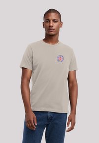 Light gray cotton t-shirt with short sleeves, featuring a round logo with a pink lion design on the chest, paired with blue jeans.
