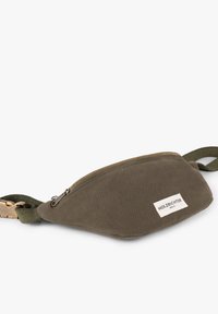Olive green canvas waist bag with a gold zipper, adjustable strap, and a front label. Rounded shape with a smooth, textured finish.