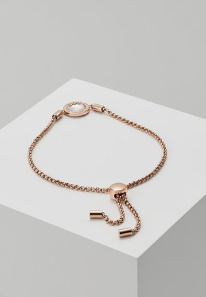 Bracelet chaîne réglable en or rose avec un pendentif rond en nacre et un fermoir coulissant sur une surface blanche.