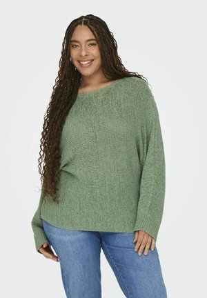 Green knit sweater with a loose fit and long sleeves, featuring a textured pattern. Paired with blue jeans.