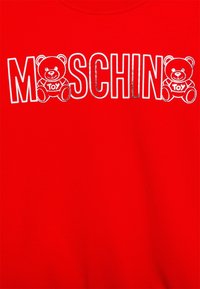 Tissu rouge avec des lettres blanches bordées spelling "MOSCHINO" mettant en scène deux ours en peluche blancs tenant des panneaux "TOY" intégrés dans le texte.