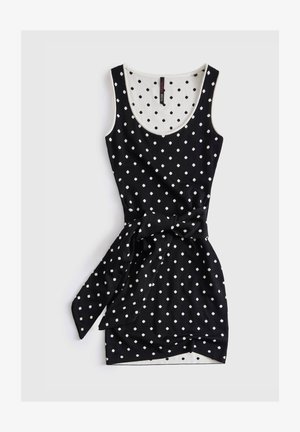 Robe noire sans manches à pois blancs, encolure dégagée, et ceinture en tissu nouée à la taille.