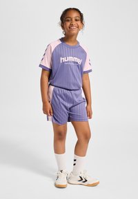 Lila und pinkes Sportoutfit mit vertikalen Streifen, kurzen Ärmeln, Shorts mit elastischem Bund und weißen Turnschuhen mit schwarzen Akzenten.