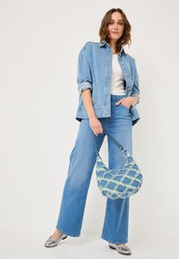 Giacca in denim blu chiaro con maniche arrotolate, abbinata a pantaloni in denim blu a gamba larga. Una borsa in tessuto blu e verde completa l'outfit.