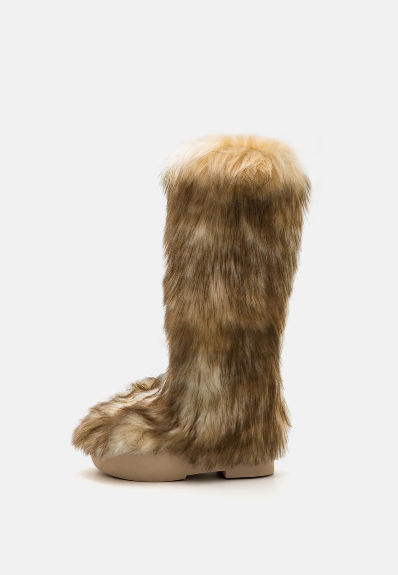 Botas altas forradas de pele, numa mistura de castanho e bege, com bico arredondado e sola plana, apresentando uma superfície suave e texturada.