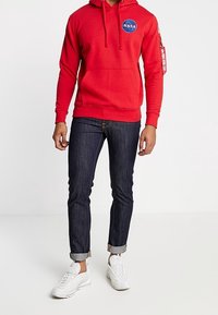 Punainen huppari, jossa on NASA-logo, etutasku ja kiristysnauhat. Yhdistetty tummiin farkkuihin, joissa on käännetyt lahkeet, ja valkoisiin lenkkareihin.