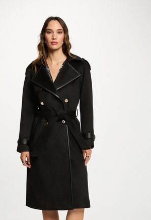 Abrigo negro de trench con diseño de doble botonadura, ribete de cuero, grandes solapas y un cinturón atado en la cintura. Textura suave con detalles de botones.