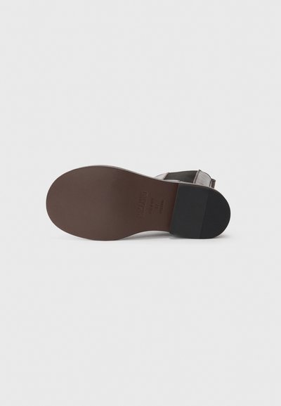 Sole di sandalo in pelle marrone con una finitura liscia. Presenta un accento in gomma nera sul tallone e il nome del brand impresso. Design minimalista.