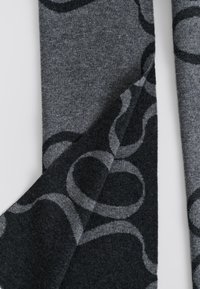 Dziany szalik w odcieniach szarości z abstrakcyjnymi wzorami kołowymi. Miękka, teksturowana tkanina z mieszanką jasnych i ciemnych tonów.