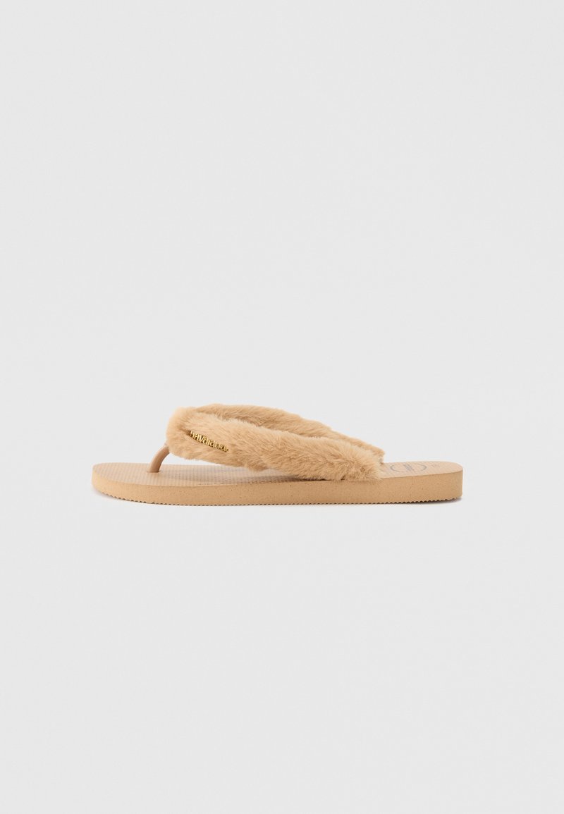 Tan spalvoti šlepetės su dirbtinės kailio juostele, tekstūruota gumine padu ir formuojamu padu. Juostelėje yra dekoratyvi auksinė detalė.