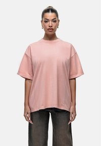 Przesadzony różowy t-shirt wykonany z miękkiego materiału, z okrągłym dekoltem, krótkimi rękawami i luźnym krojem. Widoczne detale szwów.