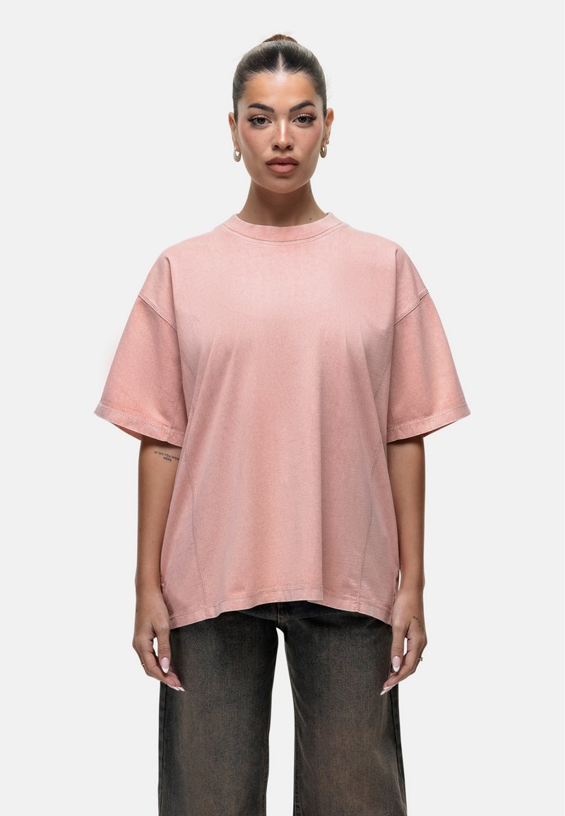 Przesadzony różowy t-shirt wykonany z miękkiego materiału, z okrągłym dekoltem, krótkimi rękawami i luźnym krojem. Widoczne detale szwów.