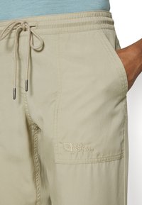 Khaki shorts tillverkade av lättviktstyg har en elastisk midja med dragsko, sidofickor och en broderad Jack Wolfskin-logotyp.