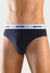 Schwarze Baumwollslips mit einem weißen elastischen Bündchen, das "Bench." in schwarzen Buchstaben trägt. Glatte Textur und figurbetontes Design.