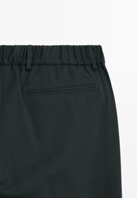 Black pants with an elastic waistband, featuring a back pocket with a horizontal seam and smooth fabric texture.