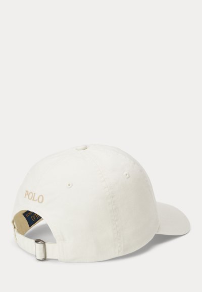 Hvit bomullslue med justerbar metallstropp, brodert "POLO" i beige på baksiden, buet skjerm og seks ventilasjonshull.