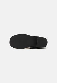 Suola di scarpa nera con una superficie liscia e piatta e texture minima. Presenta un leggero tacco e un design della punta ampia e arrotondata.