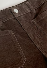 Brown corduroy pants with a textured surface, five-pocket design, and a silver button detail at the waistband.