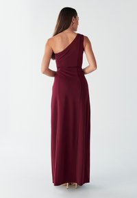 Bordo obleka na eno ramo, dolga do tal, s prilagojenim bodijem in mehko teksturo. Ima nabrano podrobnost na hrbtu za dodatno obliko.