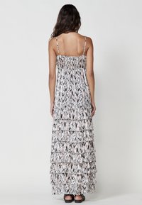 Robe maxi avec de fines bretelles, présentant un design en étages. Le tissu affiche un motif abstrait noir, blanc et rose, avec une texture légère.