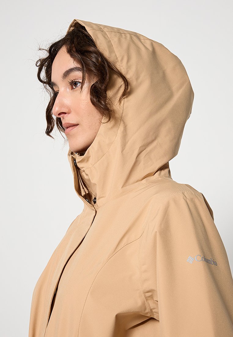 Giacca impermeabile beige con cappuccio, dotata di chiusura con zip e superficie liscia. Il logo Columbia si trova sulla manica destra.