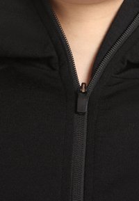 Felpa nera con cappuccio e zip frontale, caratterizzata da una texture liscia del tessuto, una cerniera metallica con una piccola linguetta di tiro e un design con colletto alto.