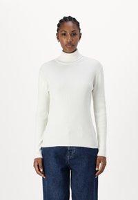 Pull à col roulé blanc côtelé à manches longues, avec une coupe ajustée et une texture douce, associé à un jean ample bleu.