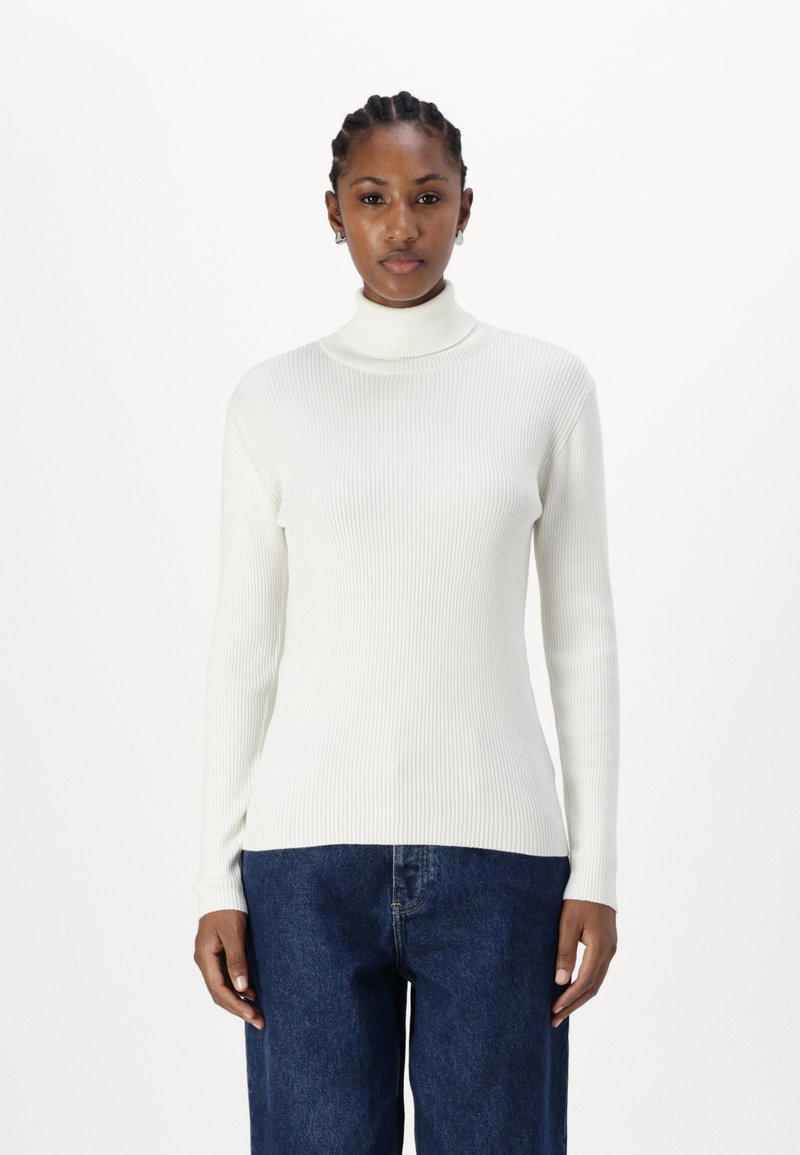 Pull à col roulé blanc côtelé à manches longues, avec une coupe ajustée et une texture douce, associé à un jean ample bleu.