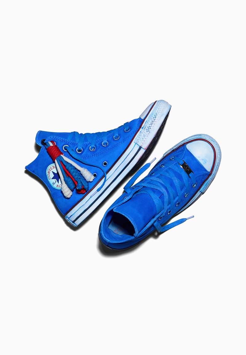 Paar blaue hohe Converse-Sneaker mit weißen Sohlen und einem rot-weiß-blauen Schnur-Schlüsselanhänger, der an einem Schuh befestigt ist.