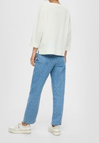 Valkoinen, tekstuurilla varustettu neule 3/4-hihoilla yhdistettynä vaaleansinisiin kuvioituihin farkkuihin, joissa on hillitty muotoilu, ja kevyet lenkkarit.