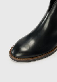 Bottes noires en cuir à talon, avec un bout arrondi, ornées d'un bord cousu marron et dotées d'une semelle en caoutchouc texturée pour une meilleure adhérence.