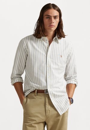 Πουκάμισο με κουμπιά σε ανοιχτό κρέμ χρώμα με φωτεινές μπλε κάθετες ρίγες; βαμβακερό ύφασμα; κανονική εφαρμογή; μακριά μανίκια που είναι ρολλαρισμένα έως τους αγκώνες; μικρή λεπτομέρεια λογότυπου.