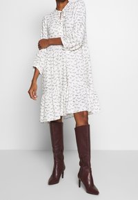 Vit utsvängd klänning med svart djurmönster, med rund halsringning och trekvartsärmar, parat med knähöga burgundy läderstövlar.