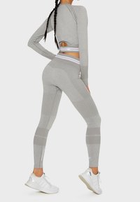 Graues Sportoutfit mit einem enganliegenden Langarmoberteil und hochgeschnittenen Leggings. Texturierte Einsätze und gestreifte Akzente werten das Design auf.
