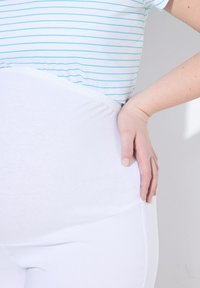 Białe legginsy z elastycznego materiału z wysokim stanem, w zestawie z niebiesko-białą w paski bluzką. Materiał wydaje się gładki i miękki w dotyku.