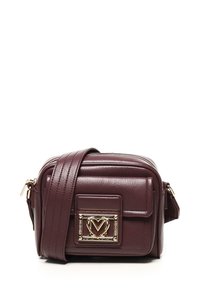 Piccola borsa a tracolla in pelle marrone scuro con tracolla larga e placca logata in metallo dorato sulla tasca anteriore.